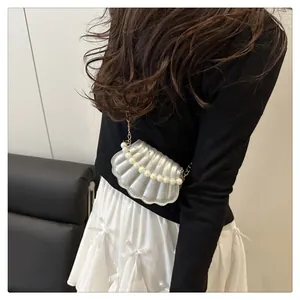 Detail of silver shell-shaped crossbody bag with pearl strap and golden chain link