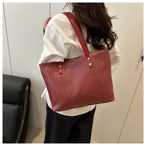 Detail of red woven tote bag with silver rivets and leather straps shown on shoulder