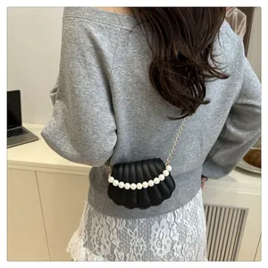 Detail of black shell-shaped crossbody bag with pearl trim and gold chain on model