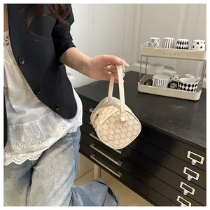 Détail de l'imprimé monogramme M sur un sac cylindrique beige porté avec un jean décontracté