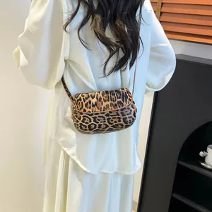 Model wearing a small leopard print saddle bag with slim strap in a cozy interior