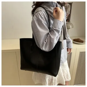 Minimalist black leather tote bag with center seam detail shown on model shoulder