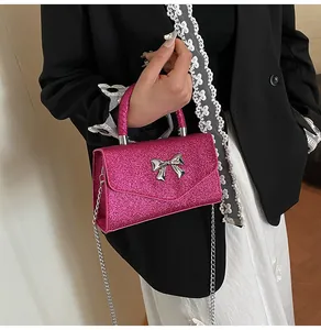 Hot pink glitter crossbody bag with silver metal bow detail shown on a female model