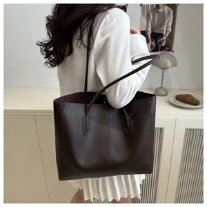 Detail view of a large dark brown leather tote bag worn by a model in a minimalist room