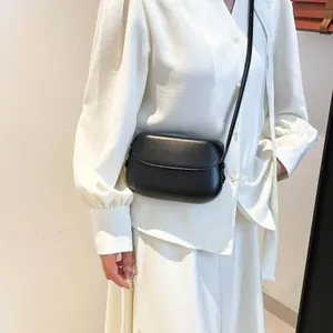 Detail of a black matte leather saddle crossbody bag worn by a model in a white studio