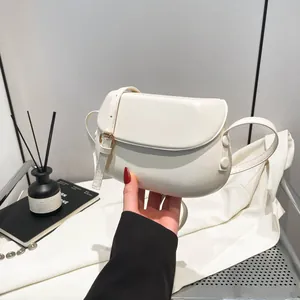 Detail of a creamy white saddle crossbody bag with adjustable strap and gold metal buckle