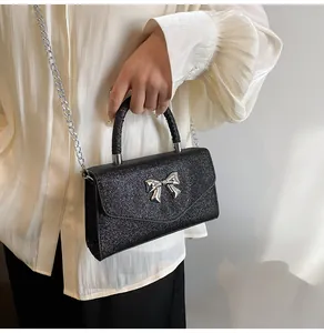 Close-up of black glitter crossbody bag featuring a silver metal bow and chain strap