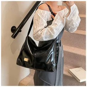 Detail of glossy black patent leather tote bag with gold logo plate and long shoulder strap