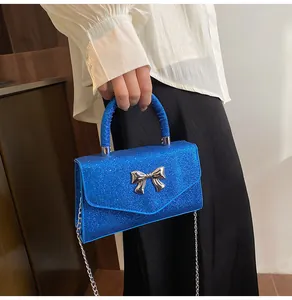 Detail of blue sequin shoulder bag featuring a silver metal bow and shiny chain strap