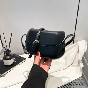Detail of a black saddle bag featuring a gold buckle and smooth minimalist finish
