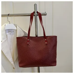 Detail view of deep red woven texture and silver rivet joints on the leather tote bag