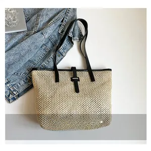 Dettaglio borsa tote in paglia intrecciata con spalline nere su sfondo denim