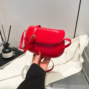 Detail of red saddle bag with smooth faux leather finish and gold buckle strap
