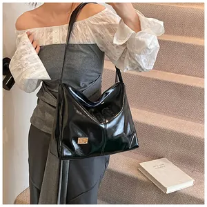 Detail of glossy black leather tote bag with gold logo plate on a lifestyle model view