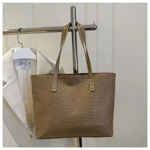 Detailed view of brown woven tote bag with metallic rivet reinforcements and dual handles