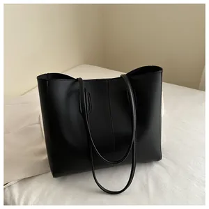 Detail of a minimalist black faux leather tote bag with vertical stitching and slim straps