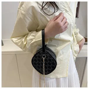 Détail d'un sac à main rond noir à monogramme avec chaîne dorée tenu par un modèle