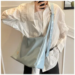 Light blue glossy leather crossbody bag with wide strap worn by a model in a white shirt