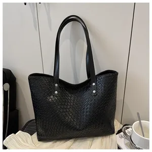 Detail of black woven tote bag featuring silver rivets on handles and premium leather texture