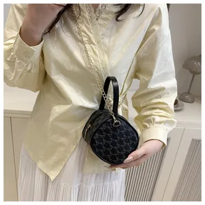 Détail d'un sac cylindrique noir avec motif M argenté et bandoulière en chaîne dorée