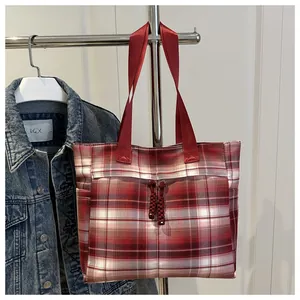 Detail of red plaid canvas tote bag with woven tassels hanging next to a denim jacket