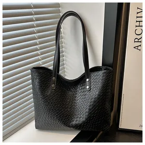 Close-up of black woven tote bag featuring leather handles and silver rivet details