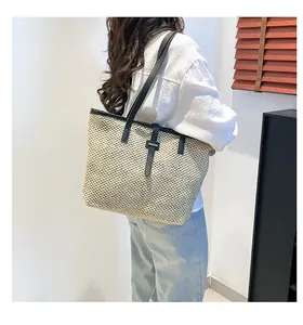 Dettaglio di una borsa tote in paglia con manici in pelle nera indossata da una modella
