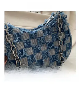 Detail view of denim checkerboard shoulder bag with frayed edges and silver chain strap