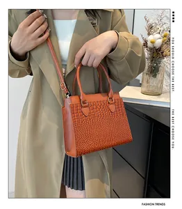 Detail of caramel brown tote bag featuring embossed crocodile pattern and gold hardware