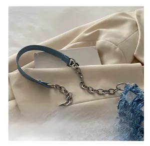 Close-up of denim shoulder bag featuring silver chain and light blue leather handle