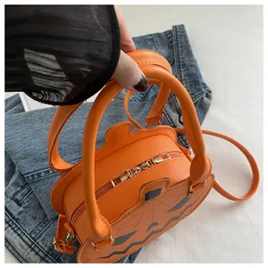 Detail of a bright orange pumpkin crossbody bag with black face and spider web print