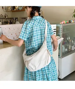 Woman wearing white corduroy crescent bag with braided zipper detail in coffee shop