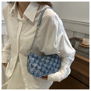 Detail of light blue checkered denim bag with frayed edges and silver chain strap