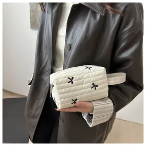 Close-up of white quilted cosmetic bag featuring black bow embroidery and fabric handle