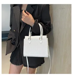 Detail of white crocodile pattern tote bag with gold hardware on a gray blazer model