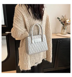 Detail der silbernen gesteppten Handtasche mit Metallic-Finish und zylindrischem Griff am Model
