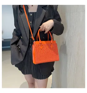 Detail of orange crocodile pattern tote bag with gold hardware on grey outfit