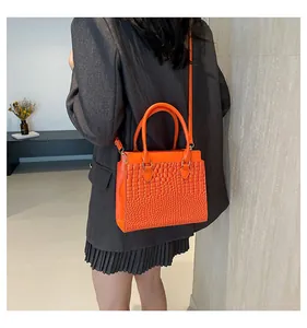 Detail of bright orange crocodile embossed tote bag with gold hardware and top handles