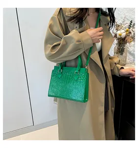 Detail of emerald green crocodile-pattern tote bag with metallic hardware and top handles