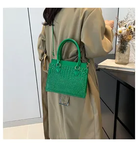 Detailed view of green crocodile texture tote bag worn over a camel trench coat