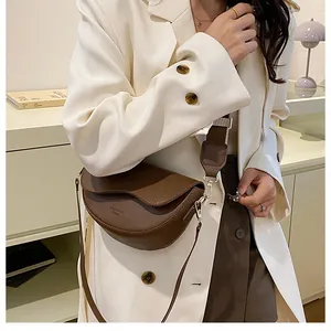 Vue latérale d'un sac selle en cuir marron mat avec large bandoulière porté par un mannequin