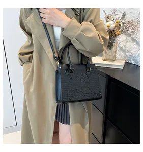 Detail view of black crocodile pattern tote bag styled on a trench coat model