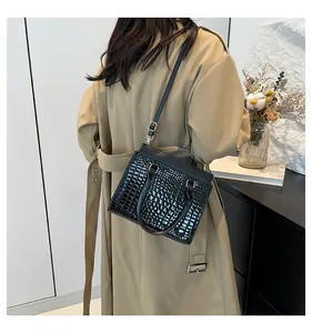 Lifestyle view of a black crocodile-embossed tote bag worn with a beige trench coat