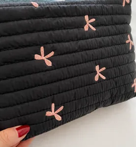 Close-up of black quilted cosmetic bag with pink bow embroidery and fine needlework details