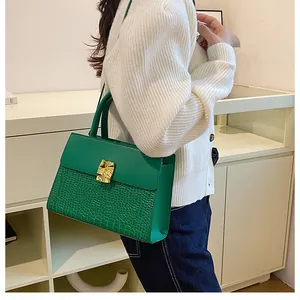 Sac à main vert avec embossage crocodile et boucle dorée présenté de profil porté par un mannequin