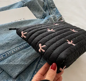 Detail of black quilted corduroy clutch with pink embroidered bow and secure zipper