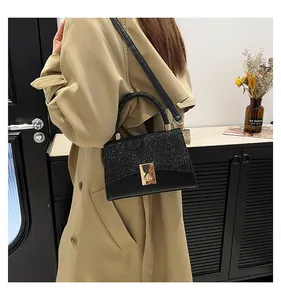 Detail showing glittery black sequin patchwork texture and golden lock on a chic square bag
