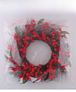 Detailed view of a Christmas wreath with red berries and green leaves in clear packaging
