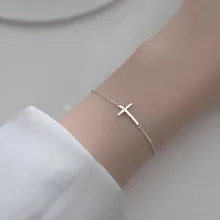Detail of silver cross pendant bracelet on wrist with fine link chain and minimalist style