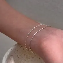 Detail view of a layered silver bead chain bracelet on a wrist with minimalist decor